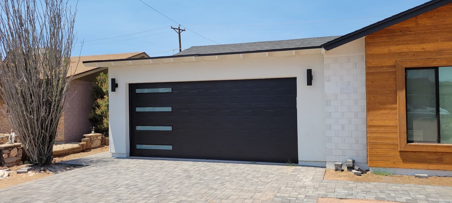 Modern black flush-panel garage door with narrow glass windows on a white desert-style home