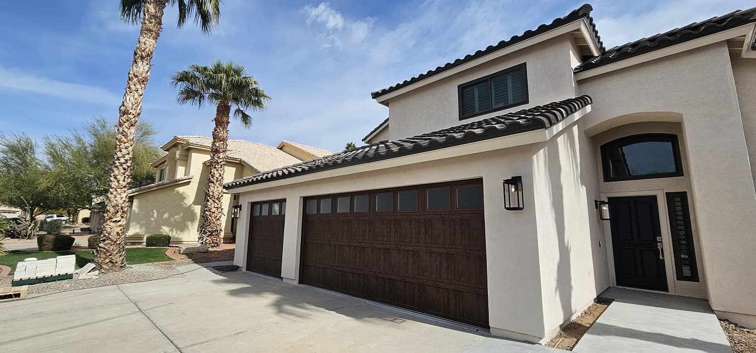 Two-story Arizona home with dark wood-look garage doors and palm trees