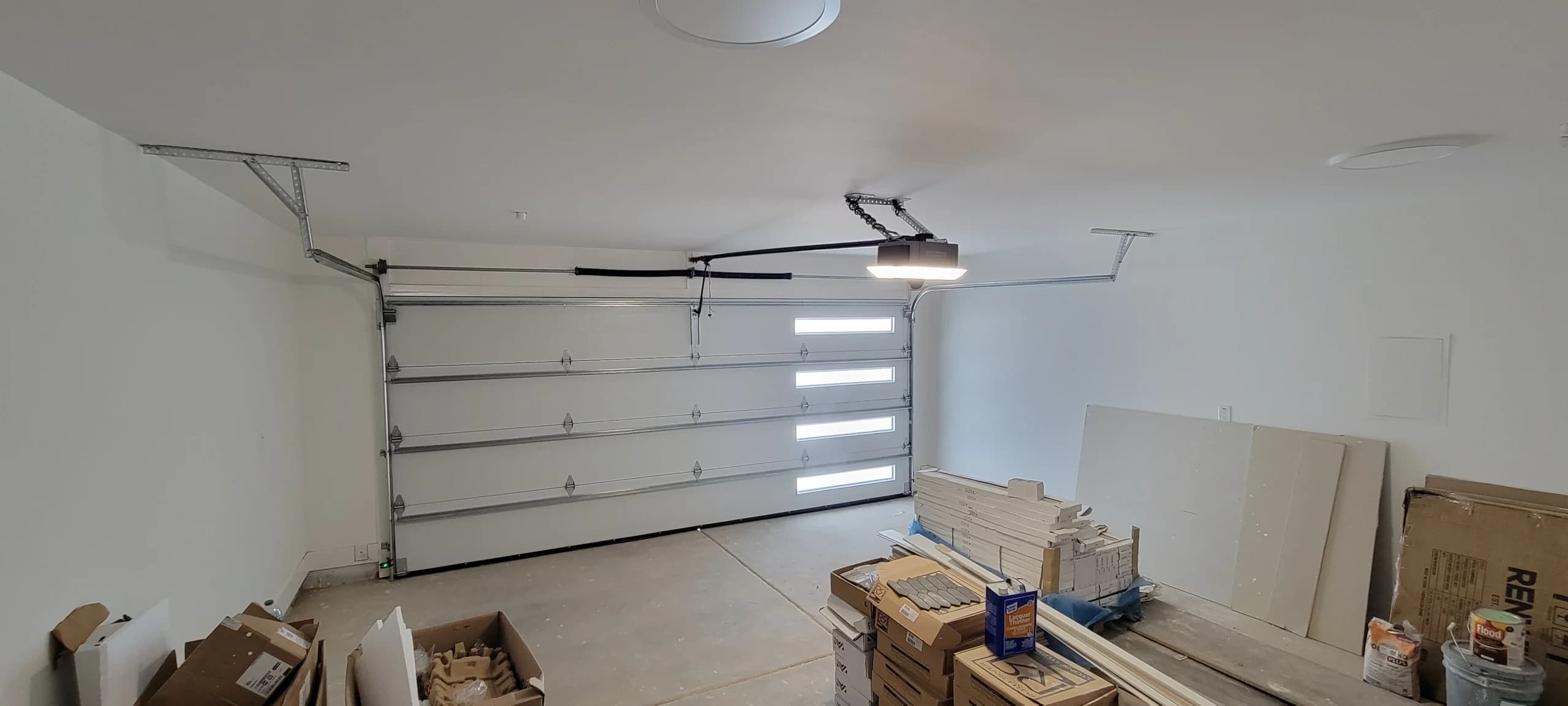 Interior view of a white steel sectional garage door with stacked frosted windows and a ceiling-mounted opener, highlighting the structural benefits of choosing steel garage doors