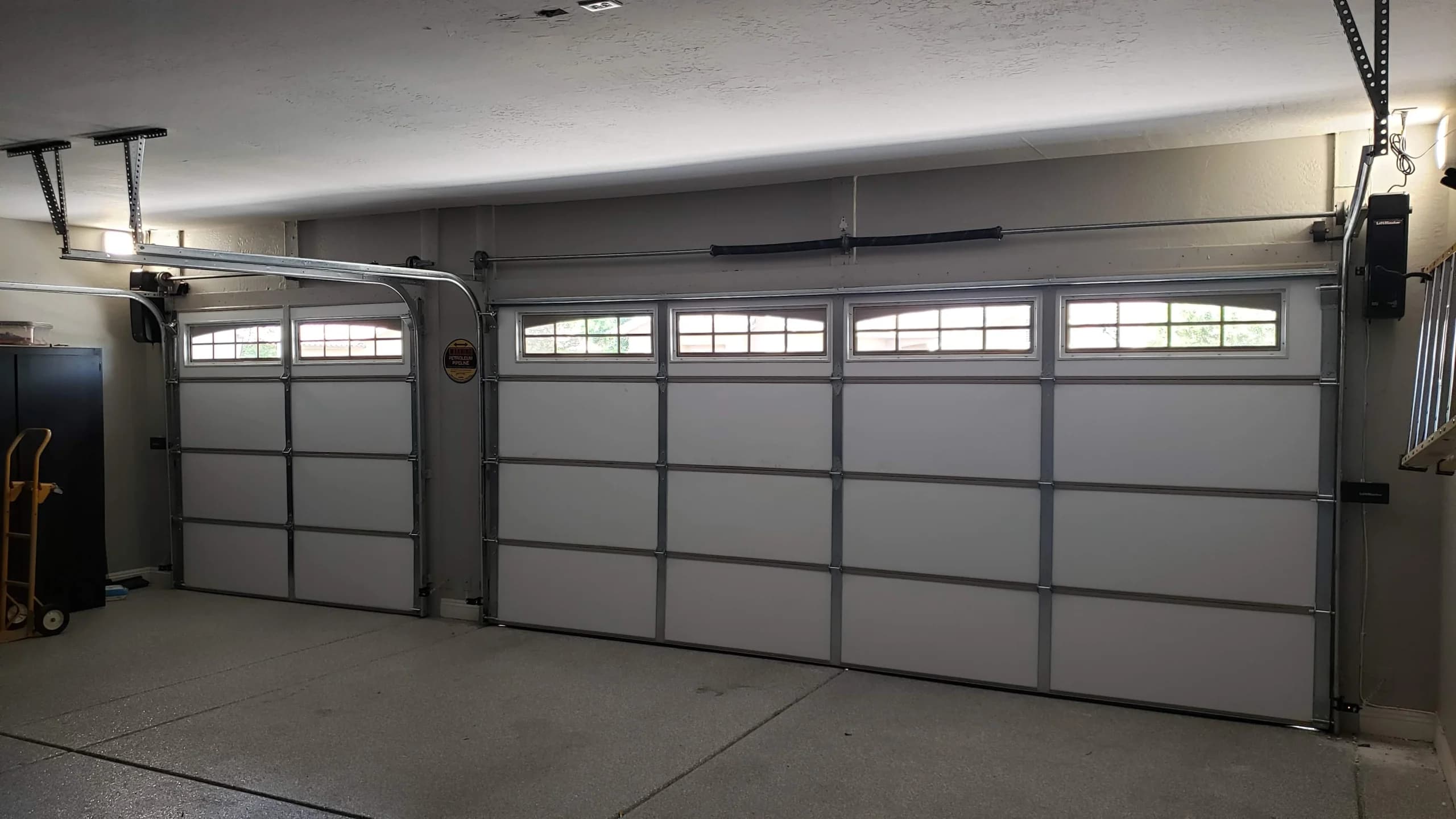 An interior view of two white sectional garage doors with arched top windows and wall-mounted openers, highlighting the hardware inspection involved in custom wood garage door maintenance