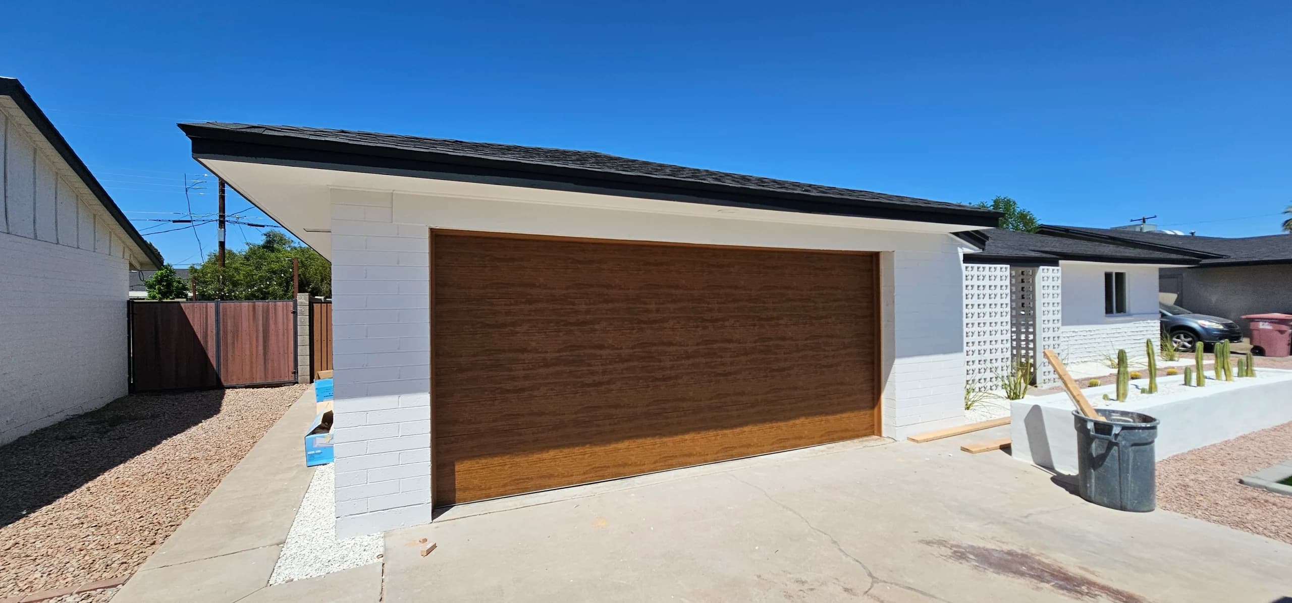 A flush, modern faux-wood garage door installed on a white brick residential home, highlighting the premium aesthetic of custom wood garage doors