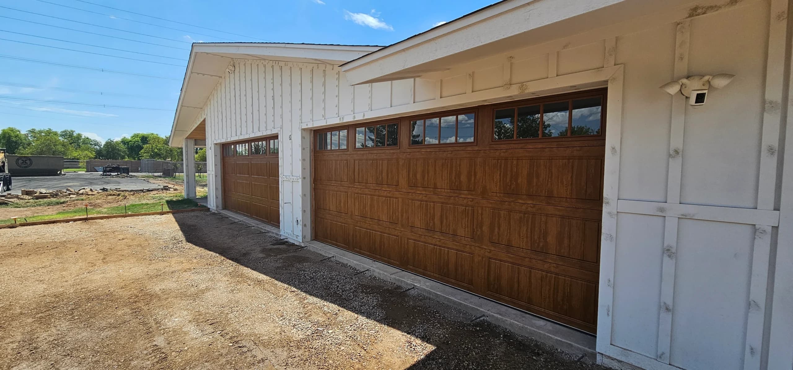 Side view of two faux-wood sectional garage doors with upper window panels installed on a white building, demonstrating the sleek design and functionality of wood grain garage doors
