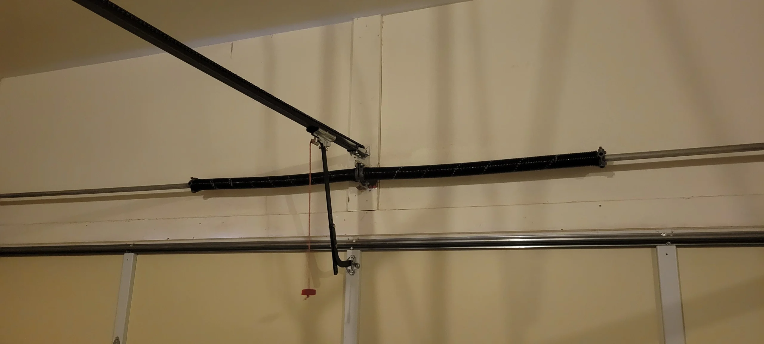 An overhead garage door mechanism showing the manual release cord used to Reengage a Garage Door After Manually Opening