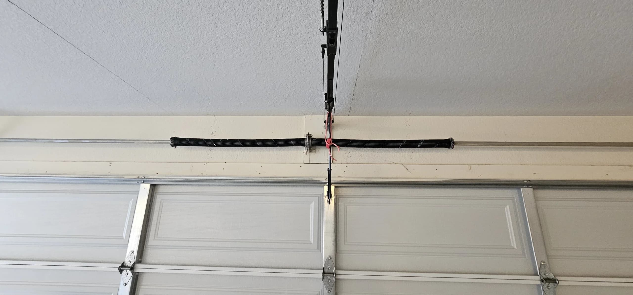 An overhead garage door track assembly highlighting the cord used for a Stuck Garage Door Emergency Release