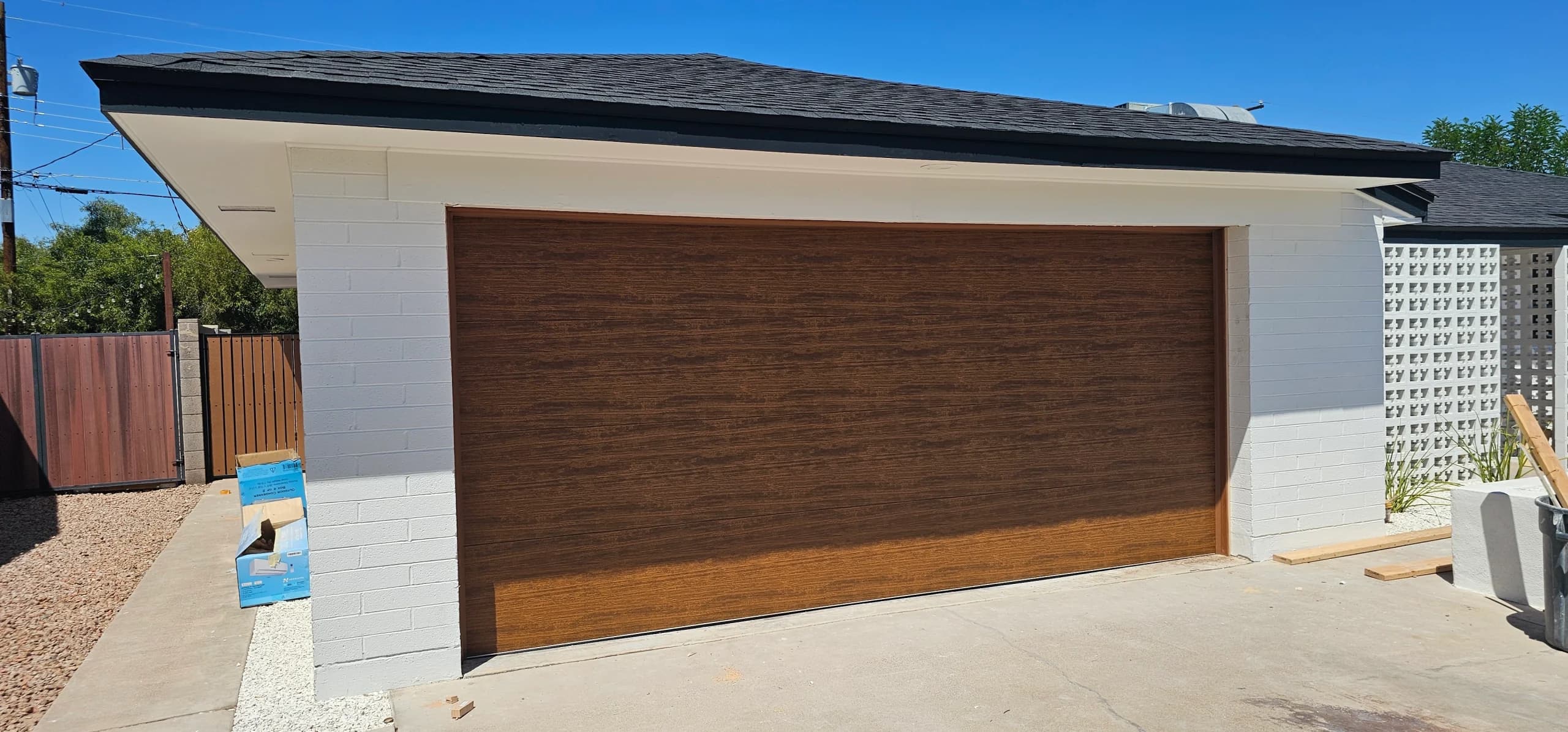 A flush, modern faux-wood garage door installed on a white brick structure, illustrating why homeowners still love wood garage doors