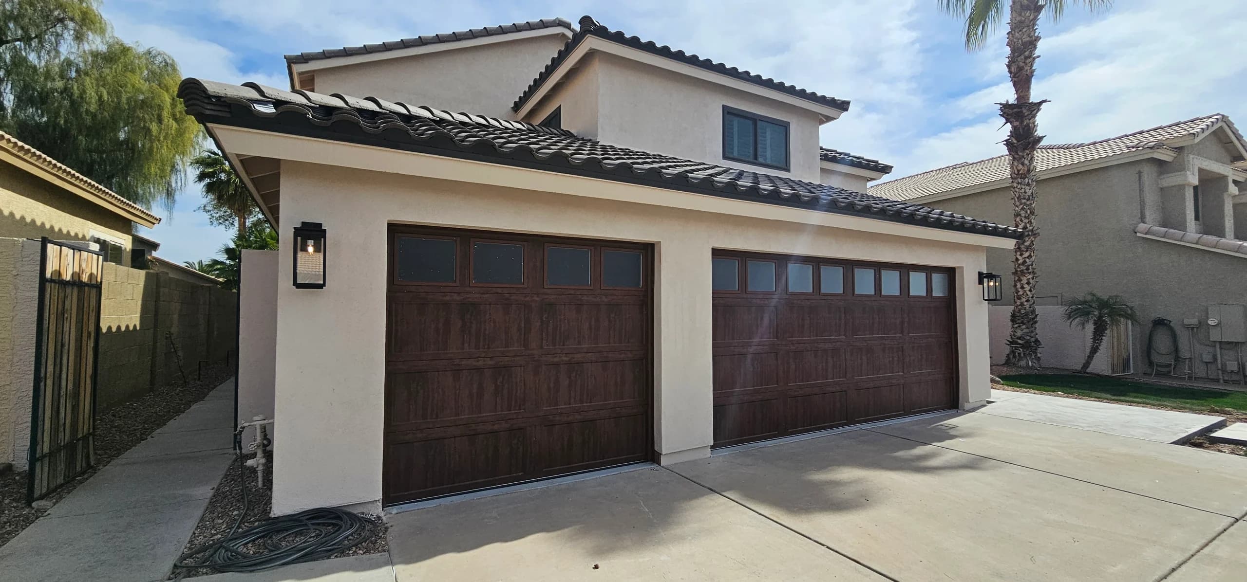 An exterior view of two dark faux-wood garage doors with square top windows on a stucco home, highlighting clean surfaces for wooden garage door panel maintenance
