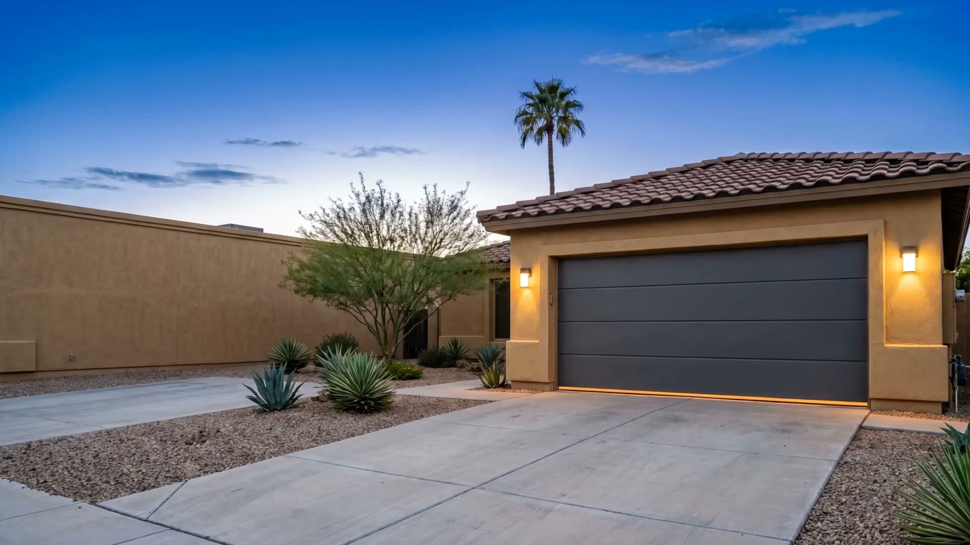 Arizona stucco home at dusk with its charcoal sectional garage door closed and warm light glowing beneath it