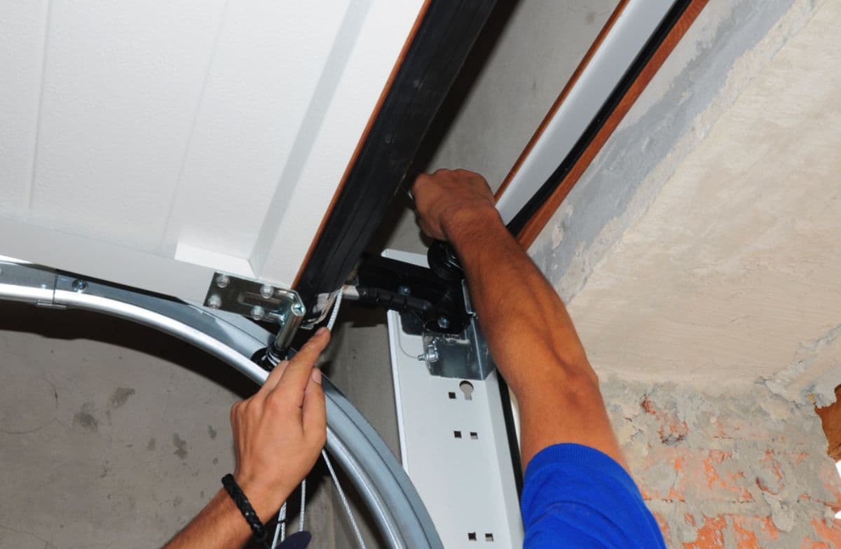 Technician's hands adjusting a garage door track and roller