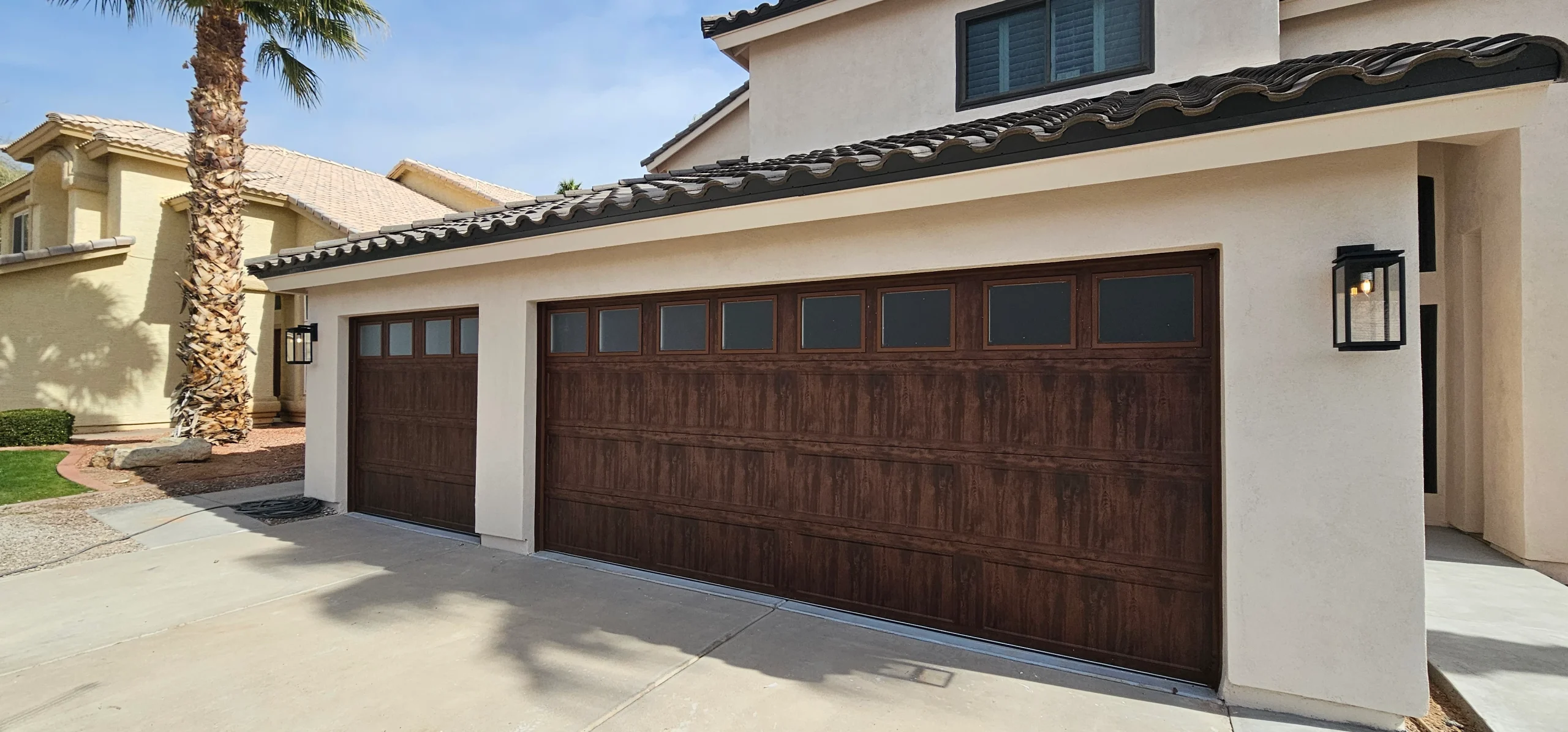 Two dark wood grain sectional garage doors with frosted top window panels on a stucco home, highlighting a sophisticated custom wood garage door design