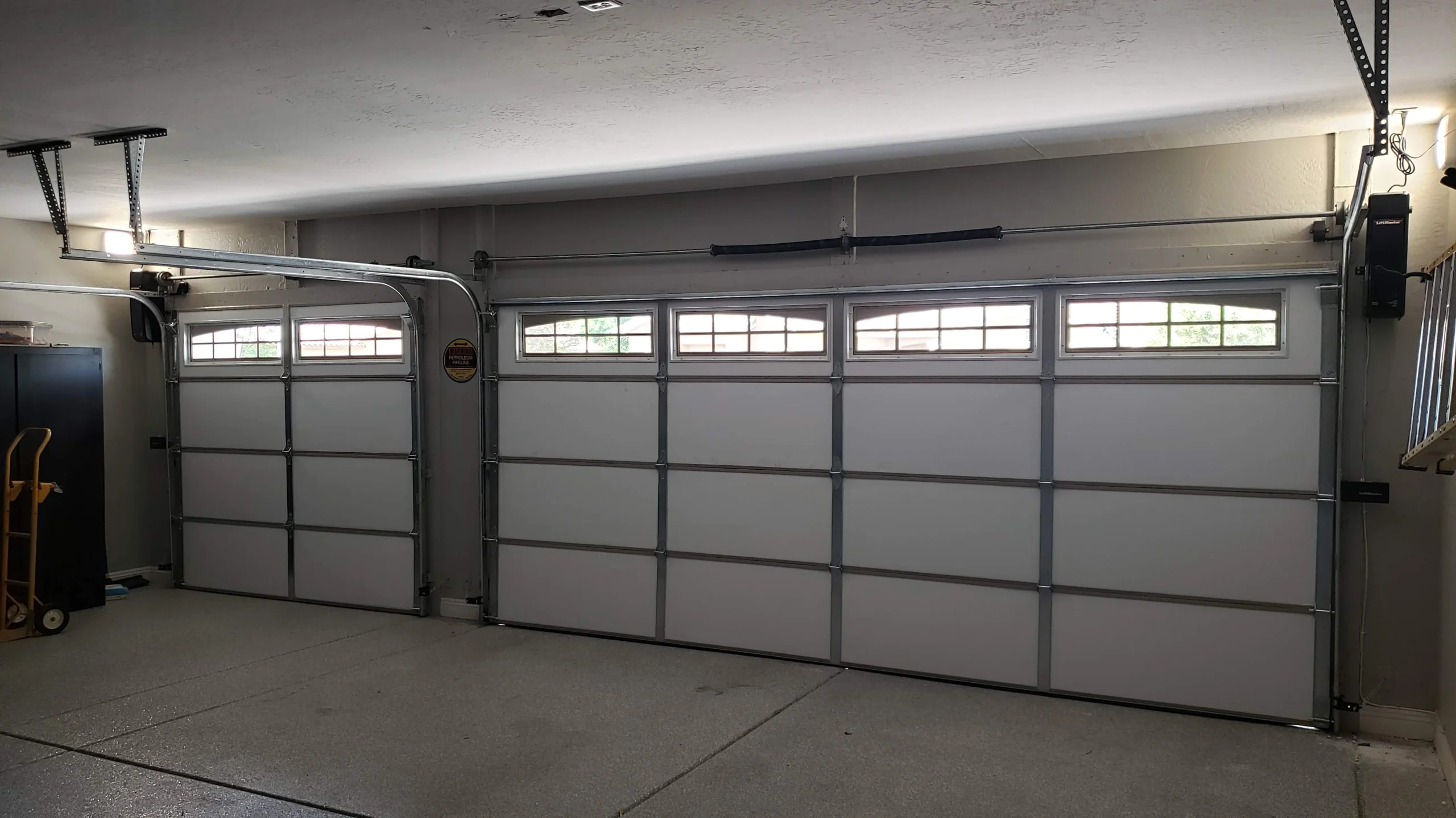 An interior view of two white sectional garage doors with arched top windows and wall-mounted openers, highlighting the hardware inspection involved in custom wood garage door maintenance