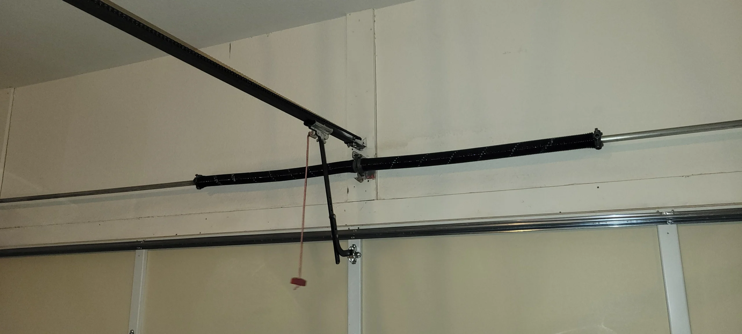 An overhead garage door mechanism displaying the emergency cord setup, illustrating a standard Garage Door Emergency Release Kit