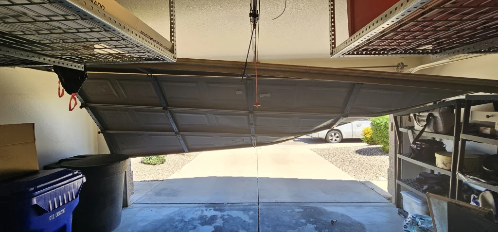 An interior view of a severely buckled and off-track garage door showing a garage door that needs professional repair
