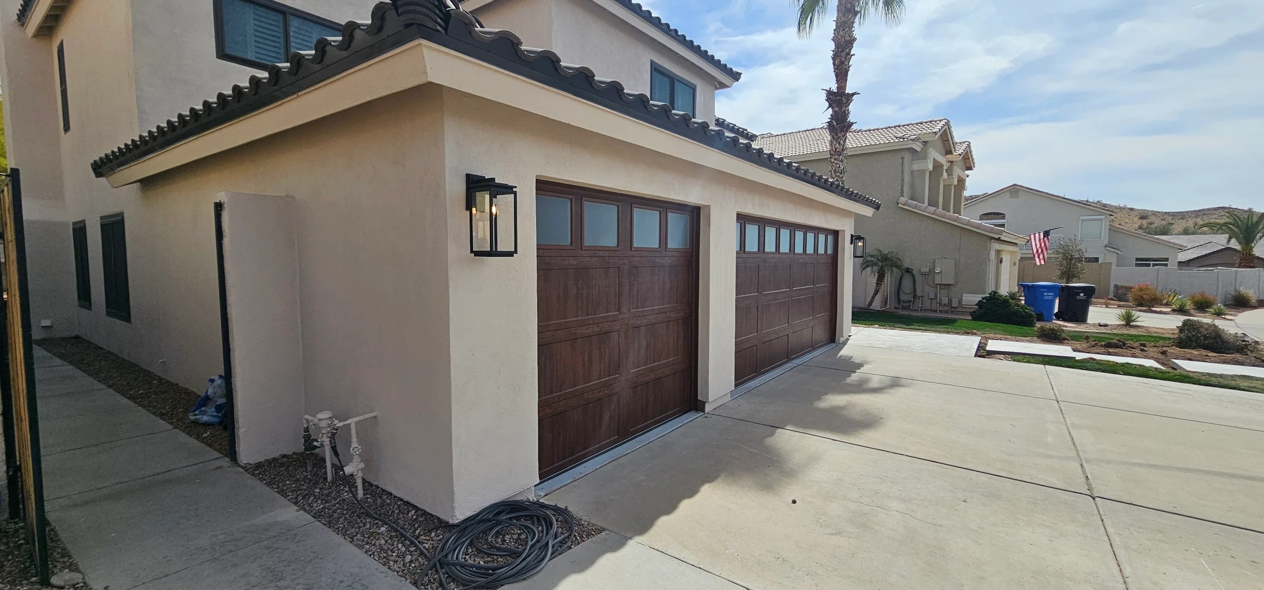 Side view of two dark faux-wood sectional garage doors with frosted top window panels on a stucco home, showcasing a sleek and modern wood garage door design