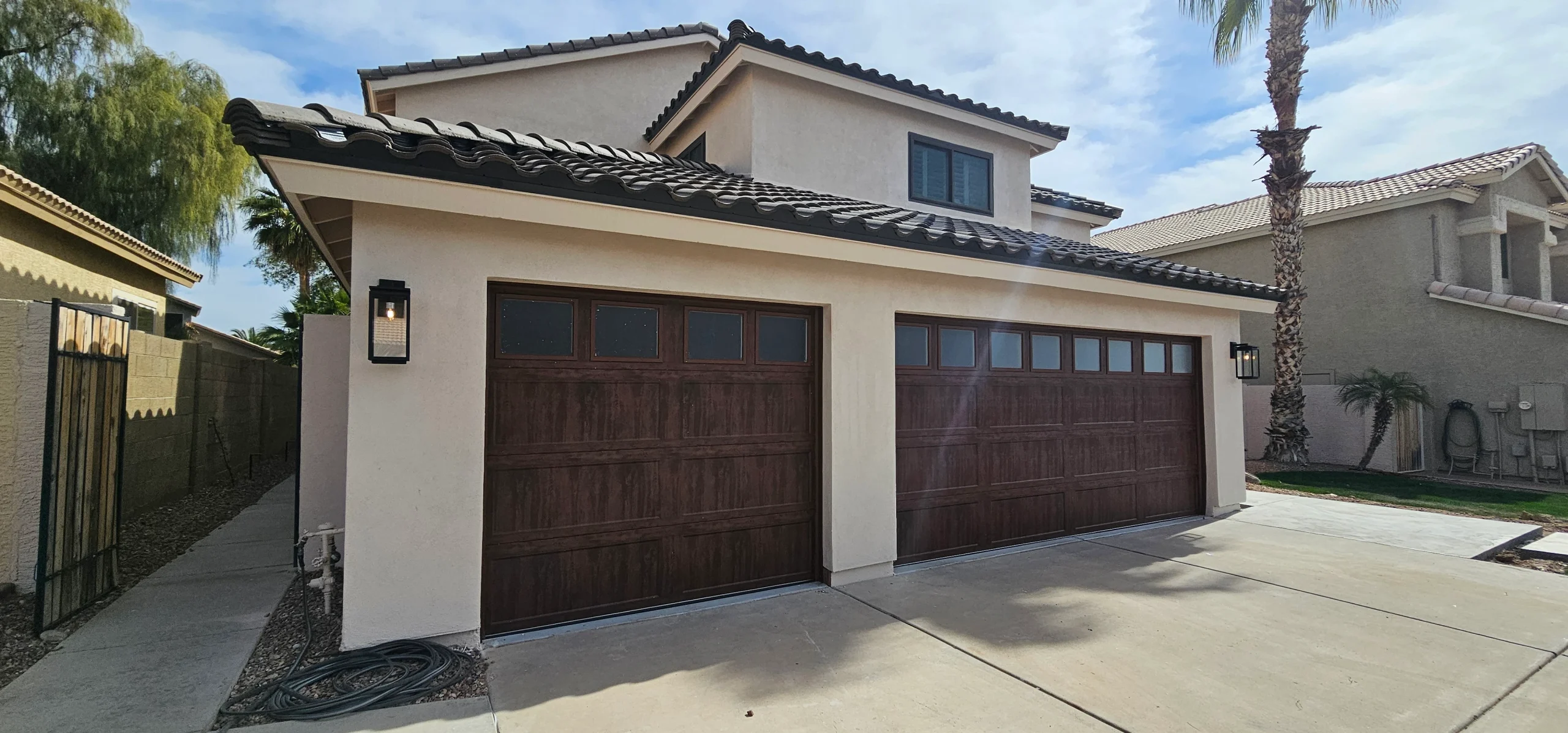 An exterior view of two dark faux-wood garage doors with square top windows on a stucco home, highlighting clean surfaces for wooden garage door panel maintenance