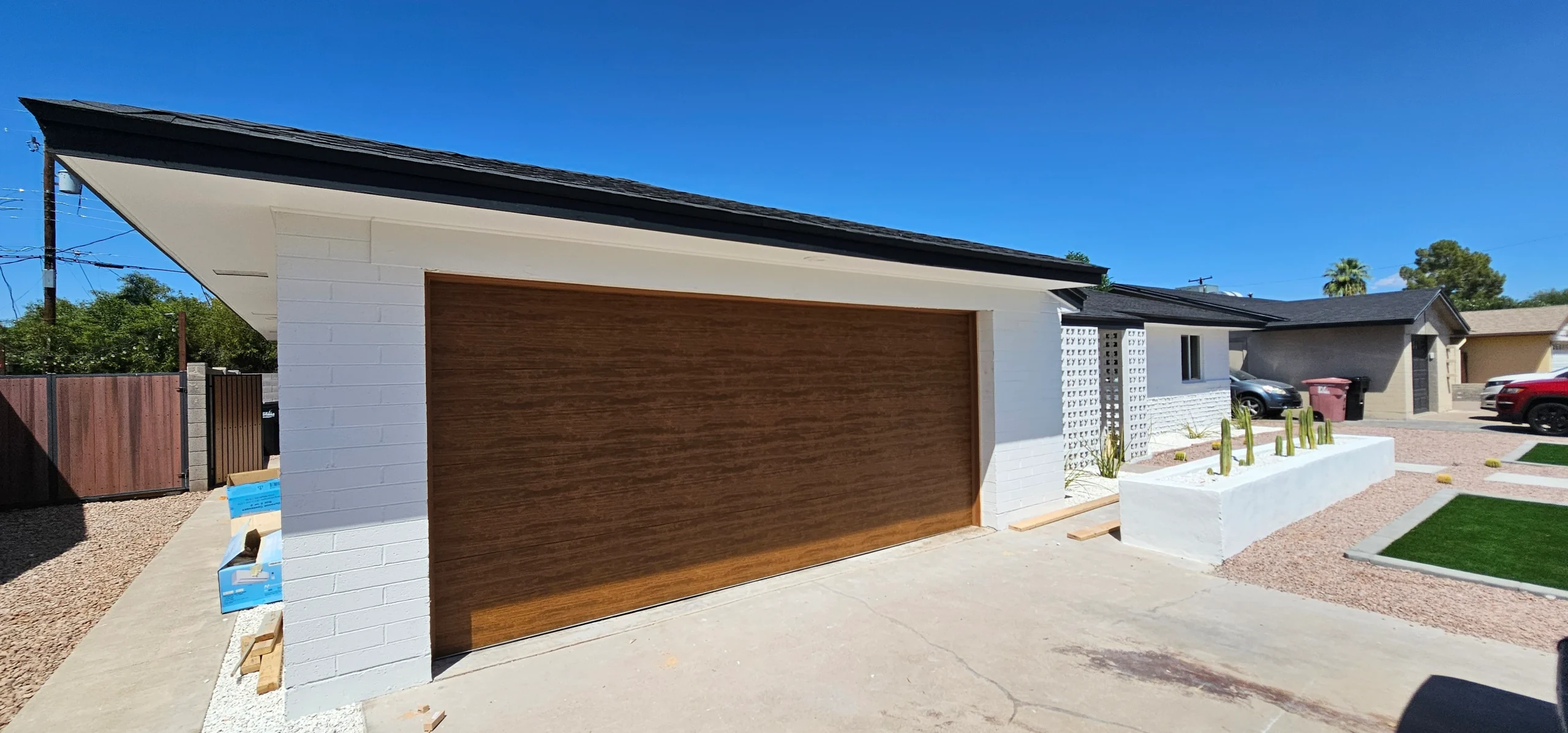 A flush, modern faux-wood garage door installed on a white brick residential home, highlighting the rich texture of wooden garage door panels