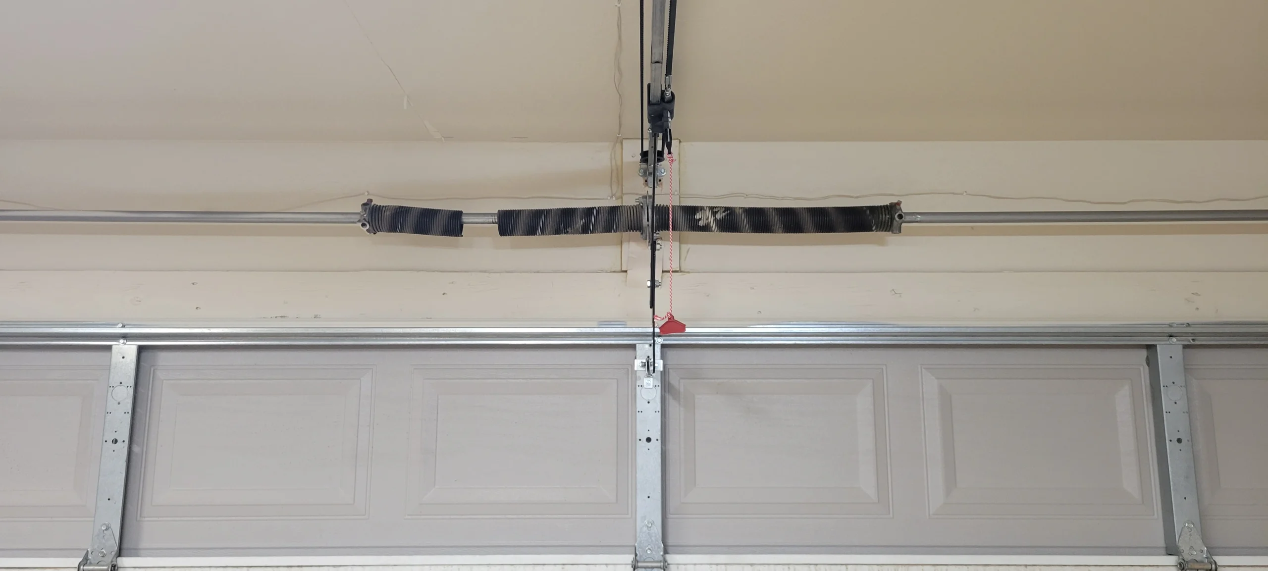 A wide view of an overhead garage door spring mechanism indicating a need for torsion spring repair.